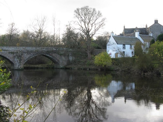 Bridge over water with a white building on the right and trees throughout.