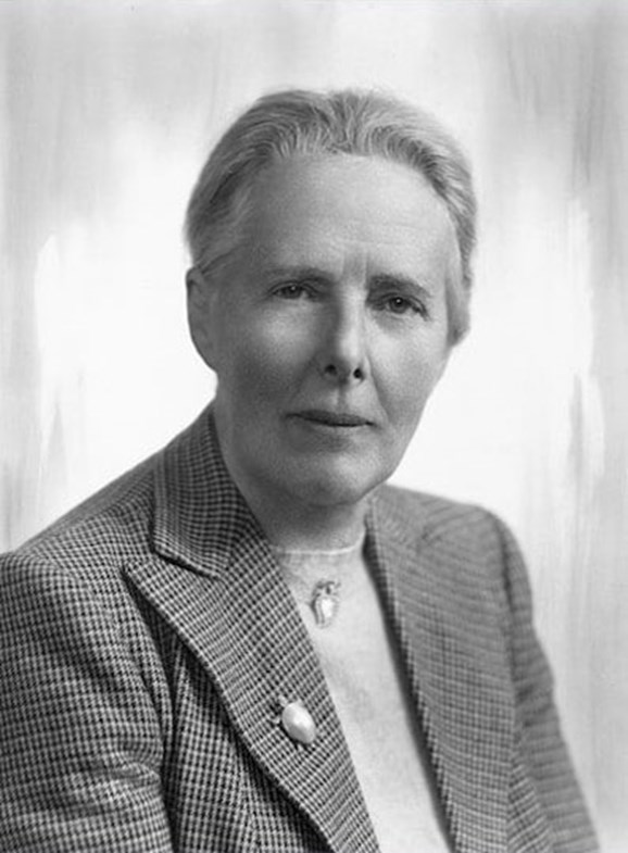 Black and white photo of a woman with short hair wearing a plaid blazer and jewelry. 