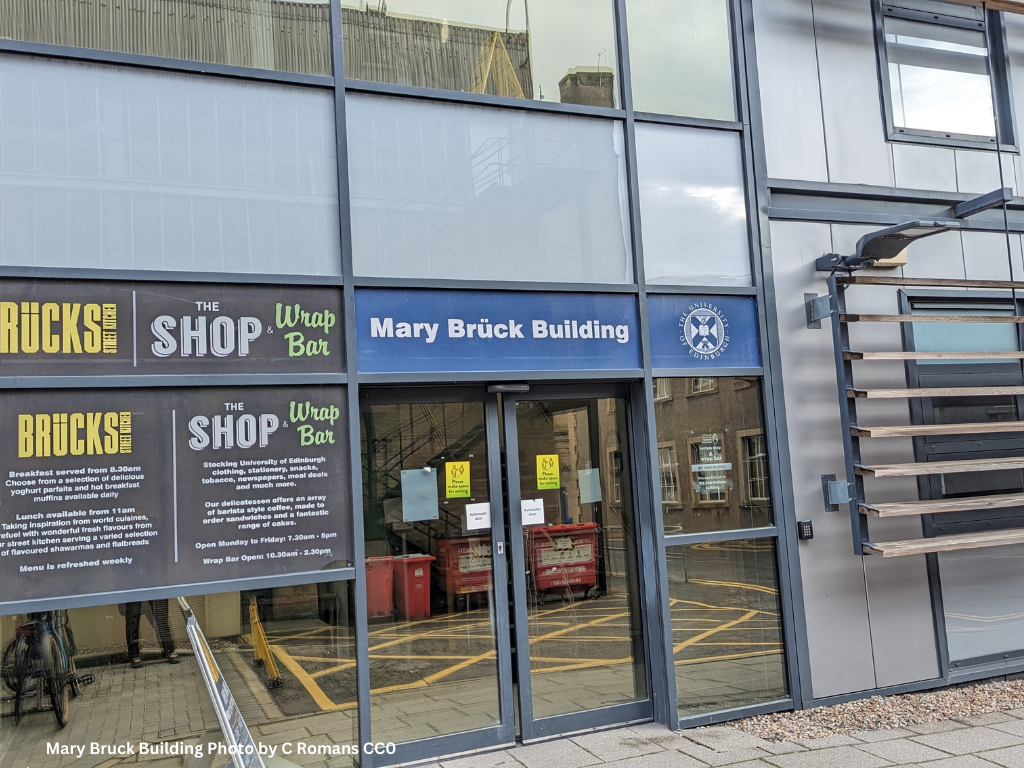 A grey, modern building with glass doors, a blue sign reading “Mary Brück Building” and a grey sign for “Brücks Street Kitchen”. 