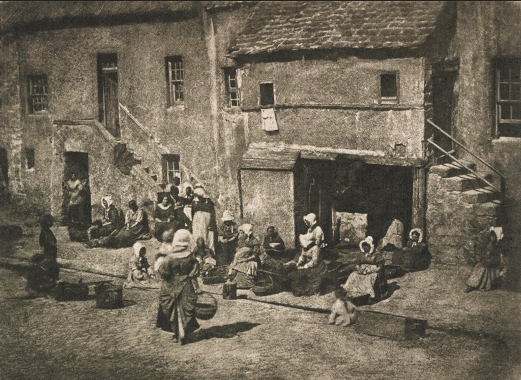 Old picture of fishery community with woman in front of houses in between baskets and fishnets