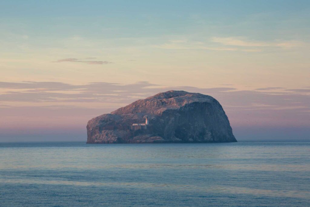 Large rock surrounded by ocean and set against sunset in the sky.