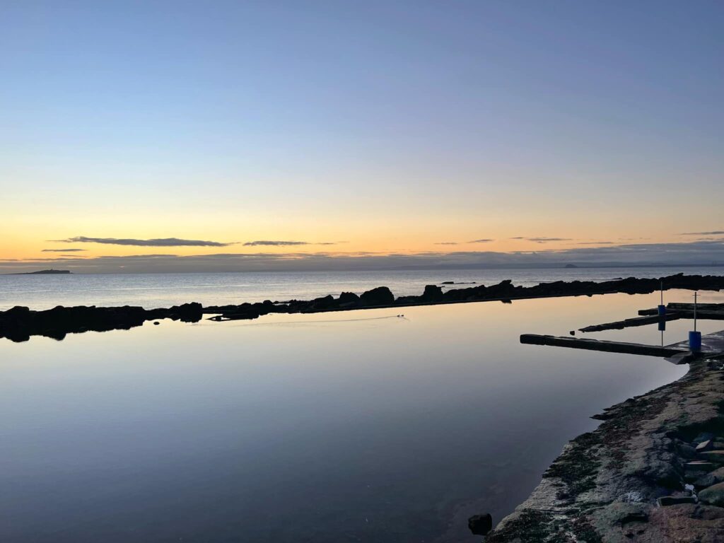 Tidal pool at sunset with the ocean and low clouds in the background.
