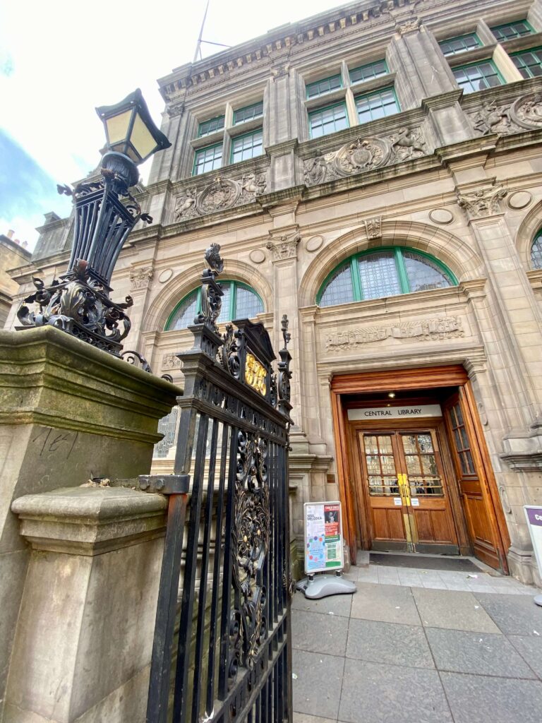 Limestone building with brown wood double door and black iron gate, sign reads Central Libray.