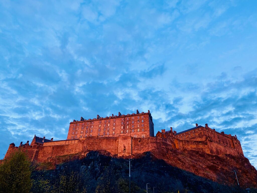 Reddish-hued castle on a rock with a blue-grey sky in the background.