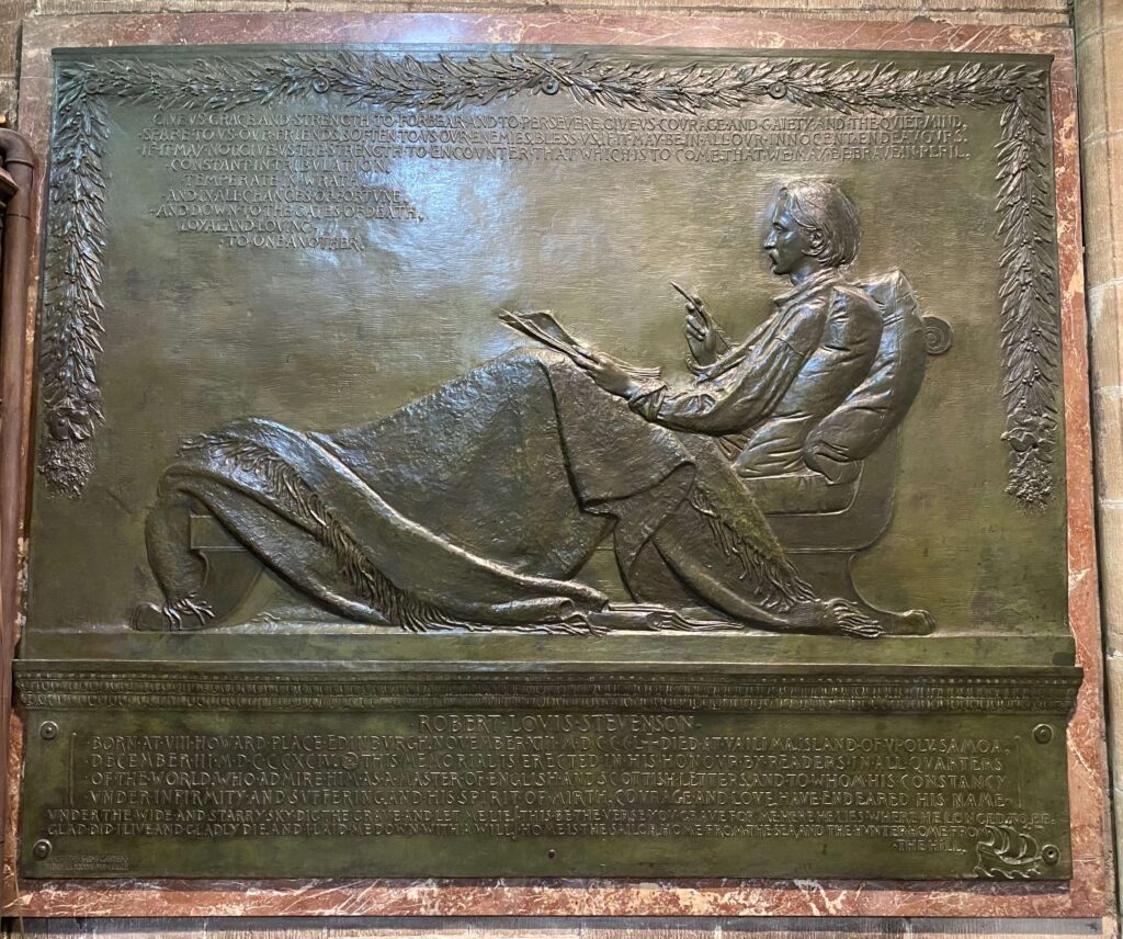 Large bronze-colored plaque showing a reclined man writing, written words, and framed by garland.