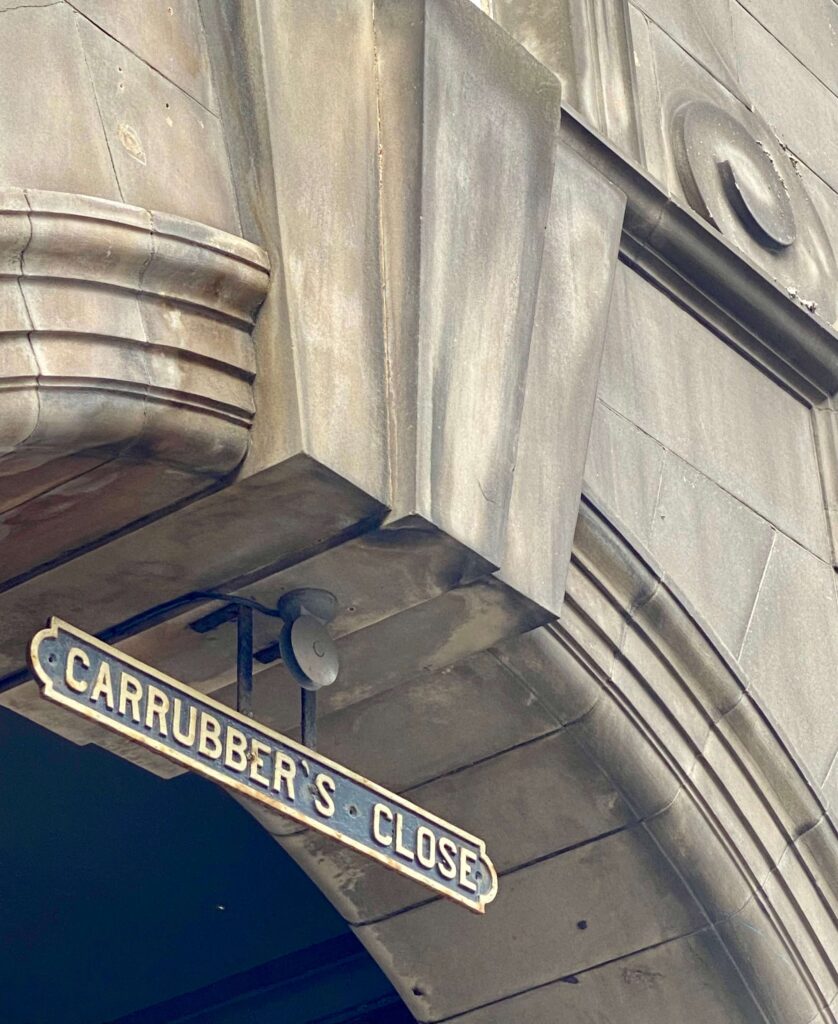 Limestone archway with hanging metal sign reading 'Carrubber's Close' in gold.