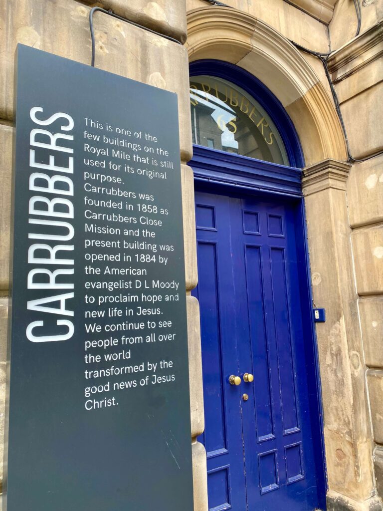 Entryway with a large sign detailing the history of the mission on the left and royal blue double doors on the right.
