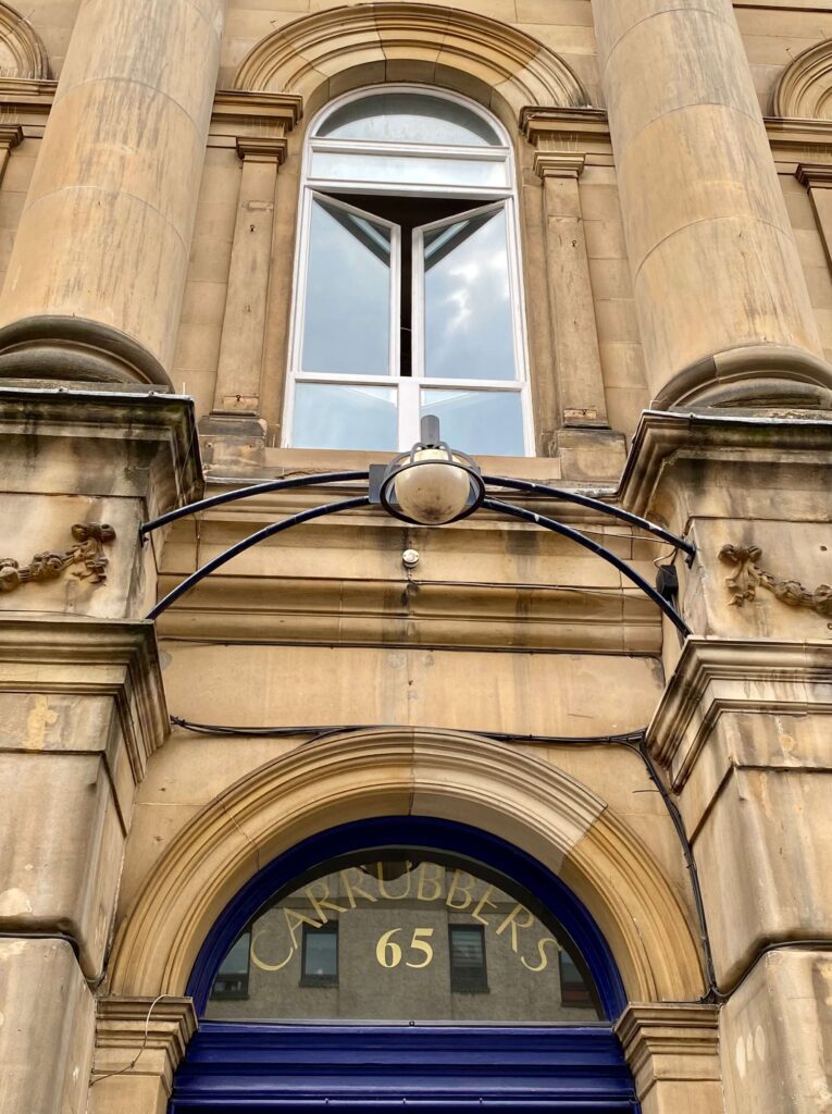 Limestone arched entryway with overhead light and windows; address reading 'Carrubber's 65.'