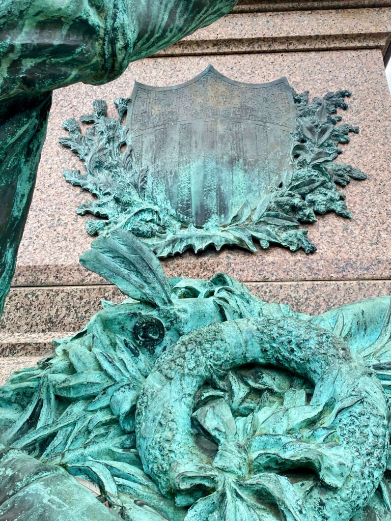 Bronze (teal) shield of stars and stripes, surrounded by metal foilage.