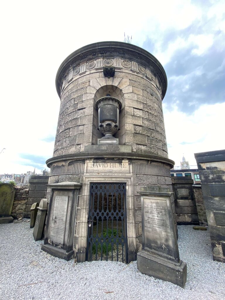 Round, tall, limestone monument with black iron gate and vase sculpture at the front; surrounded by smaller headstones and engraved with the name David Hume.