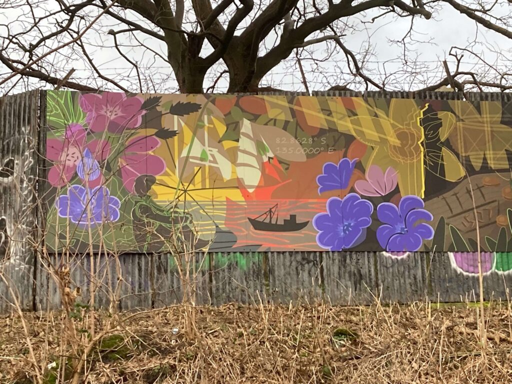 Colorful horizontal mural with purple and yellow flowers, a black boat, and seated person in front of trees with no leaves.